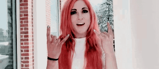a woman with red hair is standing in front of a window making a rock sign with her hands .