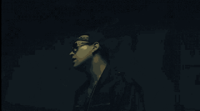 a man wearing a hat and glasses looks to the side in the dark