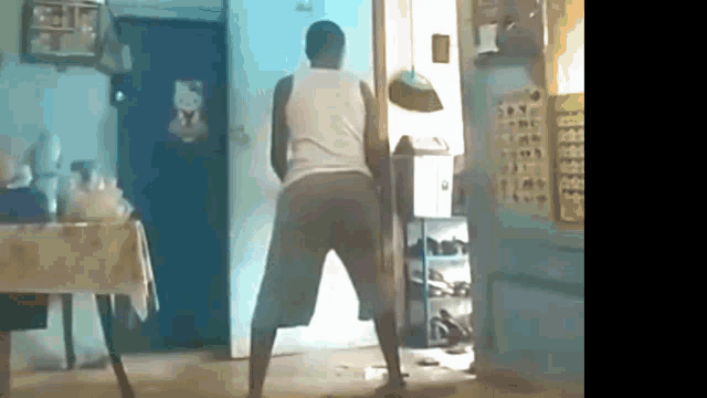 a man in a white tank top and shorts is dancing in a room .