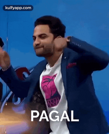 a man in a suit and a pink shirt is dancing in front of a blue wall and making a funny face .