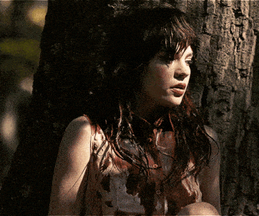 a woman with blood on her shirt is sitting next to a tree