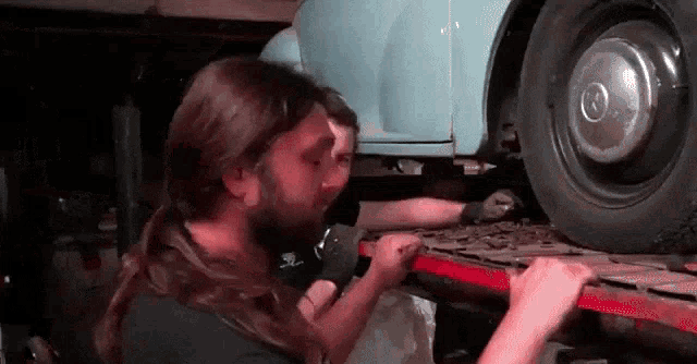 a man with long hair is working on a car in a garage