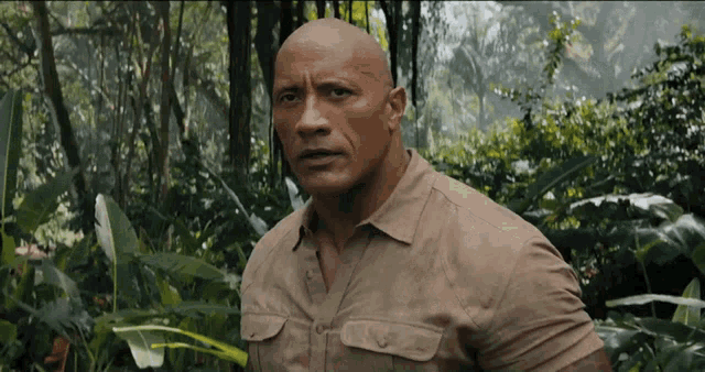 a bald man in a tan shirt is standing in the jungle