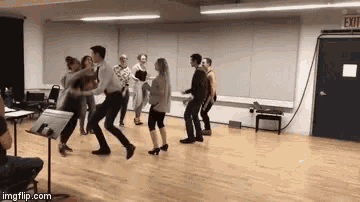 a group of people are dancing in a room with an exit sign in the background .