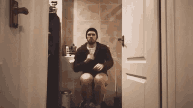 a man is sitting on a toilet in a bathroom with his legs crossed .