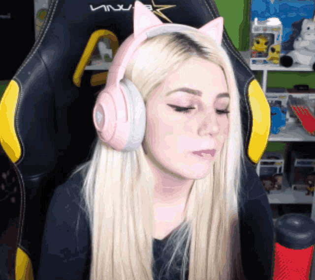 a woman wearing a pair of pink headphones with cat ears sits in a gaming chair