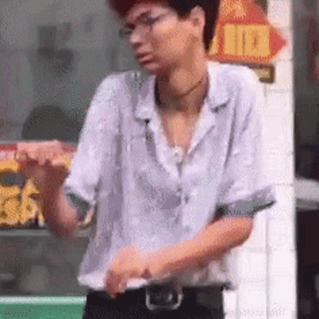 a man wearing glasses and a shirt is standing in front of a store .