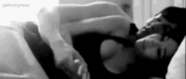 a black and white photo of a man and woman sleeping in bed .