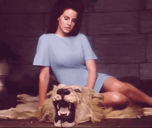 a woman in a blue dress is sitting next to a stuffed lion with its mouth open
