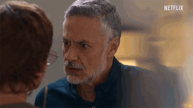 a man with a beard is looking at a woman with glasses and a netflix logo behind him
