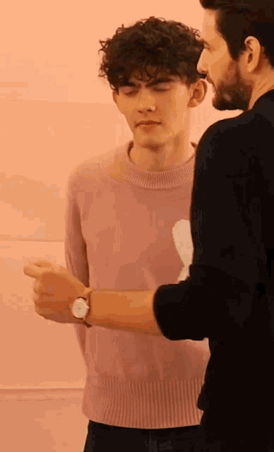 a man in a pink sweater is standing next to a man in a black shirt .