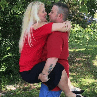 a man is carrying a woman in his arms while they kiss .