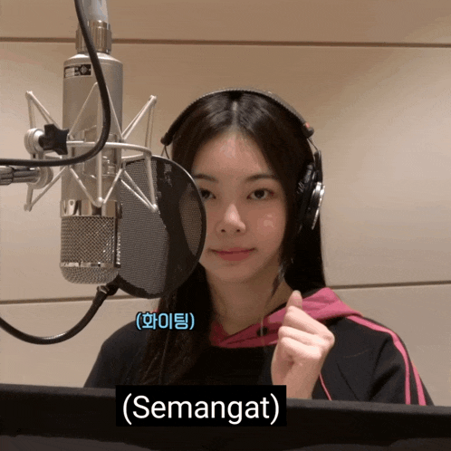 a girl wearing headphones stands in front of a microphone with a sign that says semangat