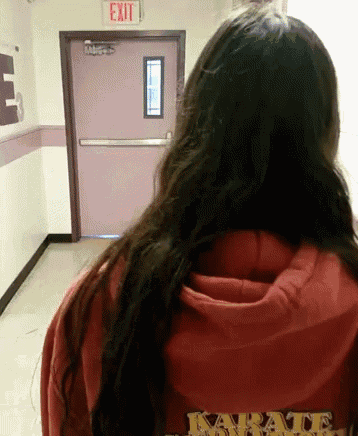 a woman in a red karate sweatshirt stands in front of a pink exit sign