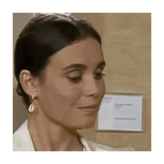 a woman wearing earrings and a white jacket looks at something