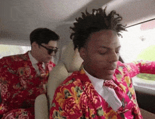 a man in a floral suit is sitting in the back seat of a car with another man