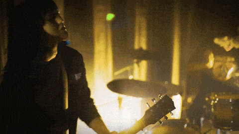 a man playing a guitar in a dark room with a drum set in the background