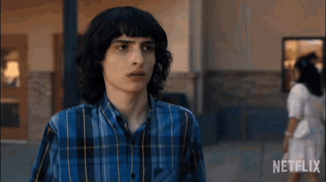 a young man in a blue plaid shirt is standing in front of a netflix sign