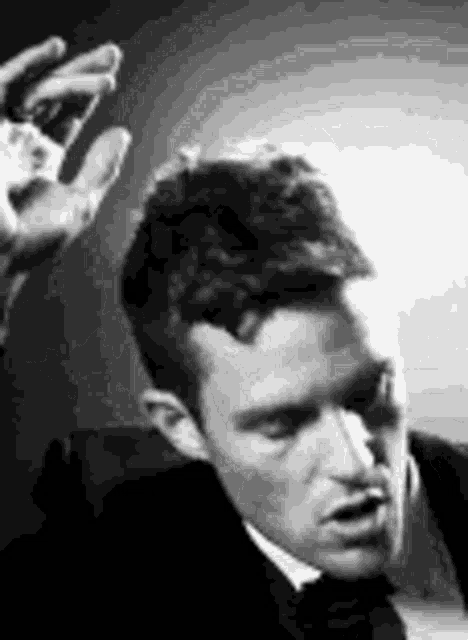 a black and white photo of a man in a suit and tie with his hands up .