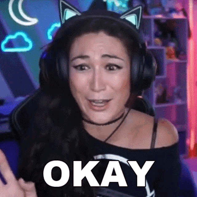 a woman wearing cat ears and headphones is making a funny face and saying `` okay '' .