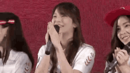 a woman is holding a microphone and smiling while sitting in front of a red background .