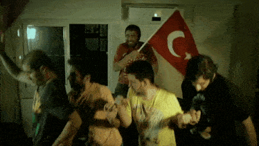 a group of men are dancing in a room with a flag that has a c on it