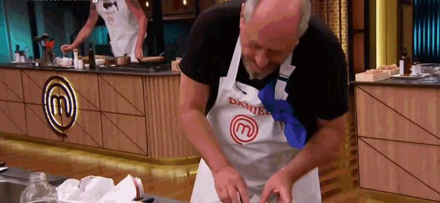 a man wearing an apron that says daniel is cutting something