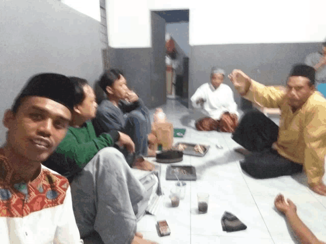a group of men are sitting on the floor and one man is wearing a yellow shirt