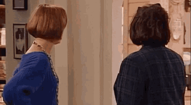 two women are standing next to each other in a hallway .