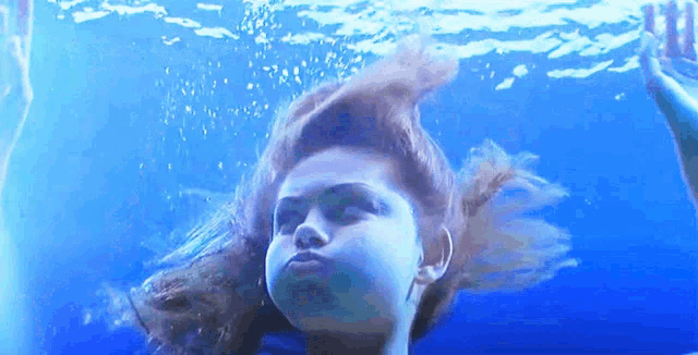 a woman is swimming underwater and making a face