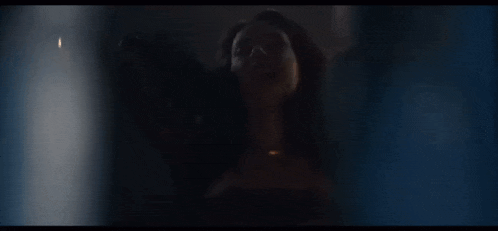 a woman is standing in a dark room with her eyes closed and a candle in the background .