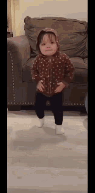 a little girl is standing in front of a couch wearing a polka dot hoodie