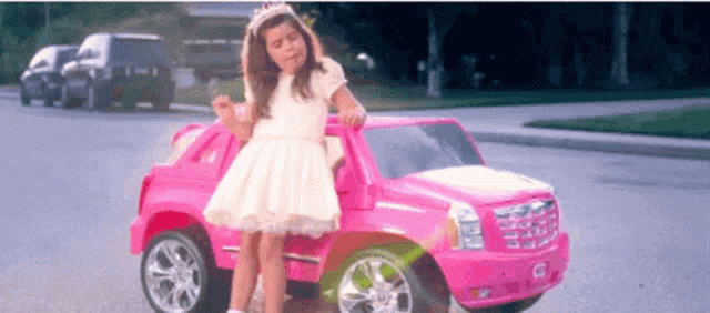 a little girl is sitting on a pink toy car