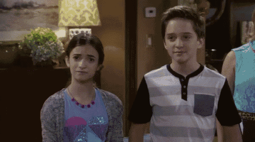 a boy and a girl are standing next to each other in a living room looking at each other .