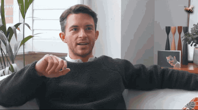 a man in a black sweater is sitting on a couch with his arm outstretched