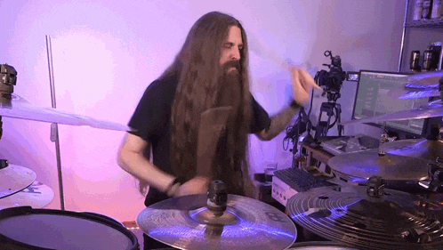 a man with long hair and a beard is playing a drum set .