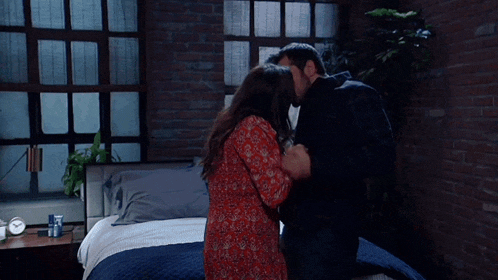 a man and a woman are kissing in a bedroom with a brick wall