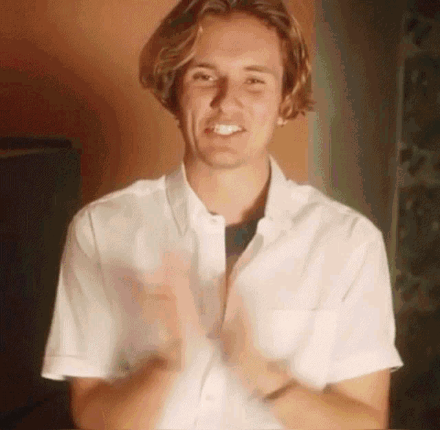 a young man wearing a white shirt is clapping his hands in a room .