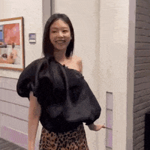 a woman wearing a black one shoulder top and a leopard print skirt is smiling .
