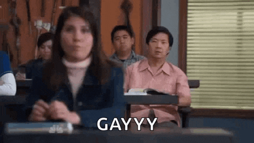 a woman is sitting at a desk in a classroom with other people and making a funny face .