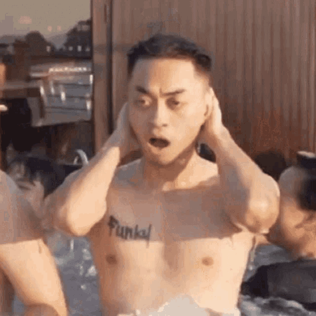 a shirtless man with a tattoo on his chest is standing in a hot tub with his hands on his ears .