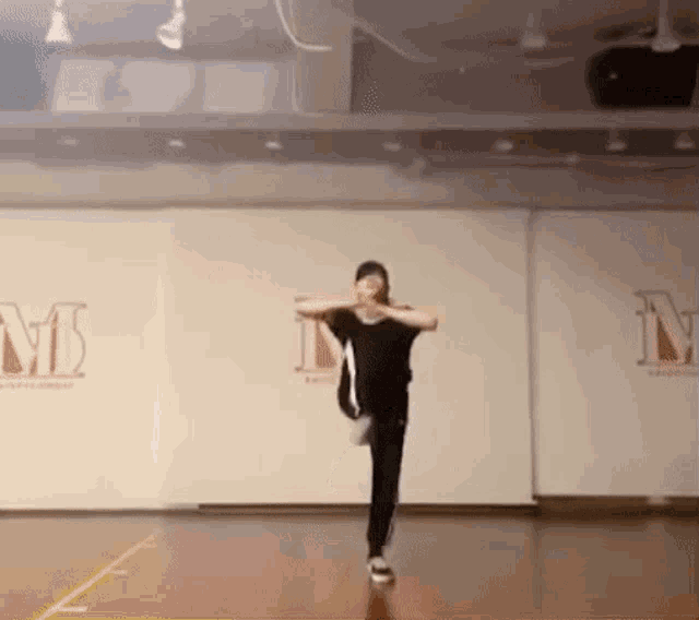 a person is dancing in a dance studio with the letter m on the wall behind them .