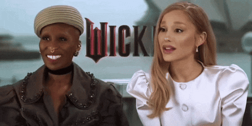 two women are sitting in front of a sign that says " wick "