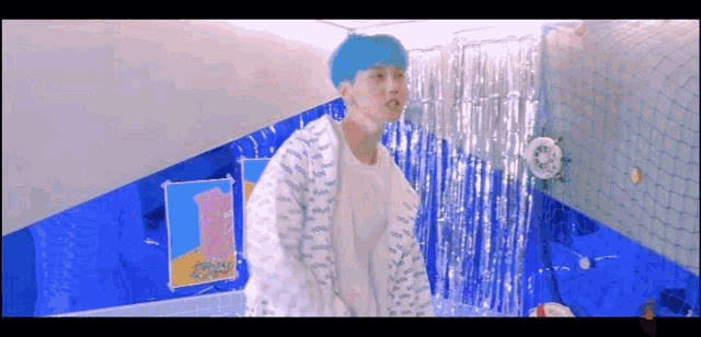a young man with blue hair is standing in a room with a blue wall .