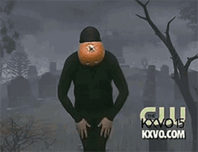 a man with a pumpkin on his head is standing in front of a cemetery