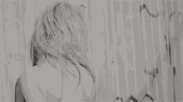 a black and white photo of a woman standing in front of a wall .