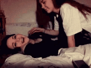 two girls are laying on a bed laughing and playing with each other