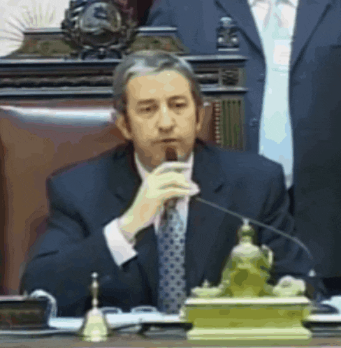 a man in a suit and tie is sitting at a desk with a microphone in his hand