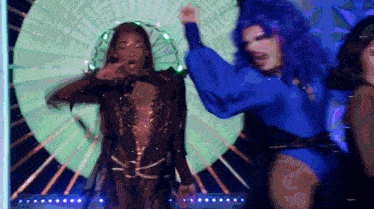 two drag queens are dancing on a stage with a green circle in the background