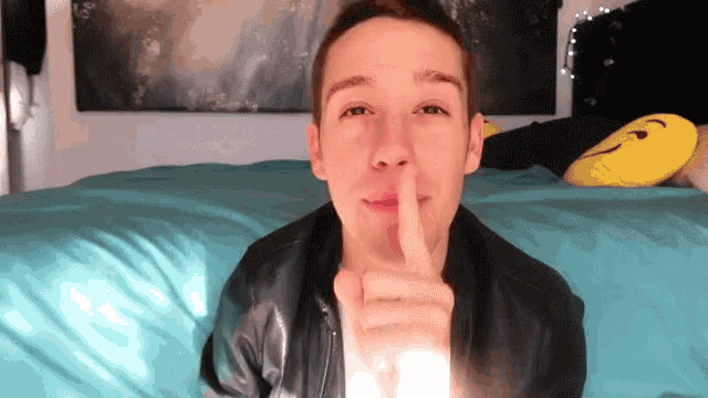 a young man laying on a bed making a shhh gesture